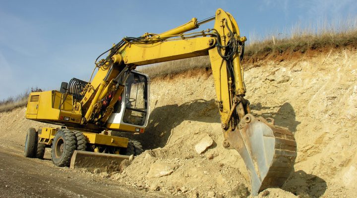 A large yellow wheeled excavator actively digging and shaping a steep earthen slope under a clear blue sky, demonstrating powerful earthmoving capability.